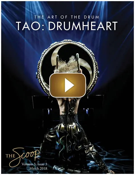 A performer plays a large drum on stage under dramatic lighting.