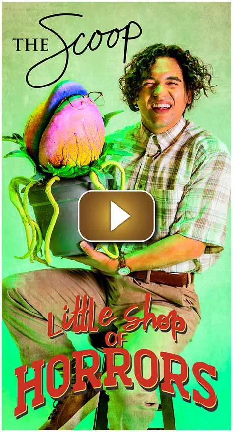 Man holding a large, colorful flower prop with 'Little Shop' text.