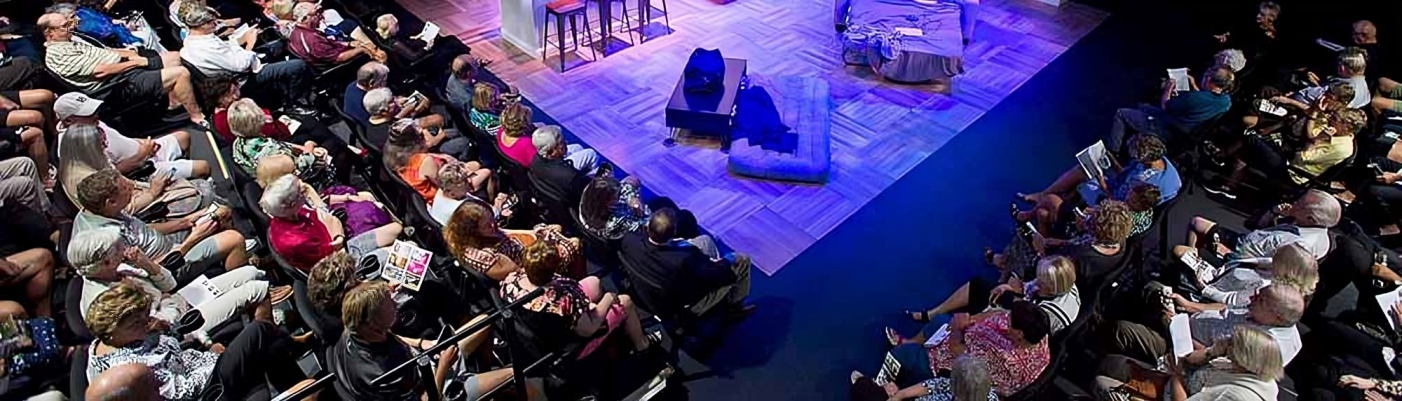 Audience watching a theater performance with a stone prop on stage.
