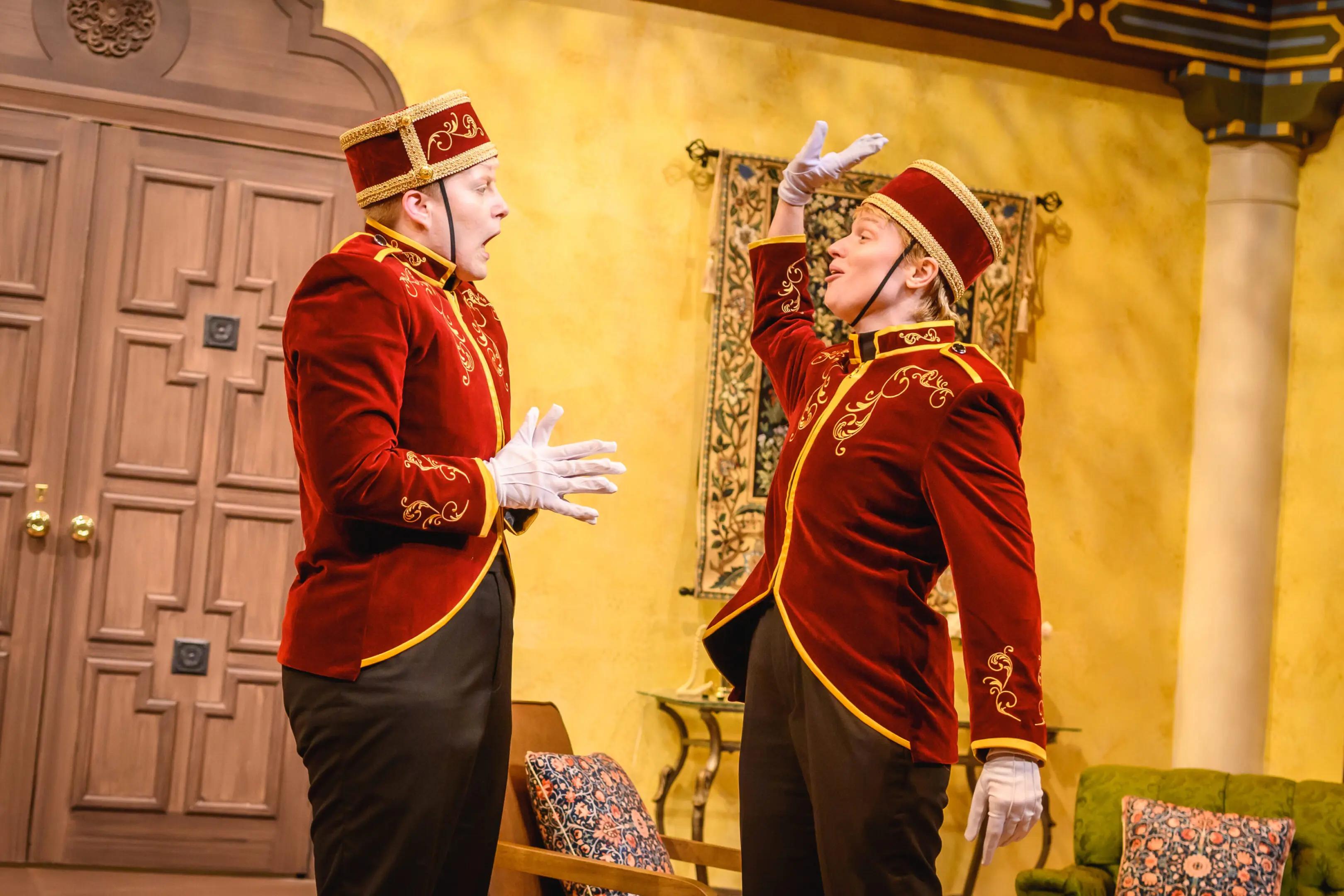 Two men in red velvet uniforms having an intense conversation indoors.